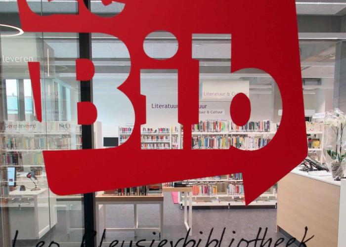 Op deze afbeelding van de Leo Pleysierbibliotheek zie je door het glas de boeken van de bib. Je ziet ook het logo van het bib op het glas.