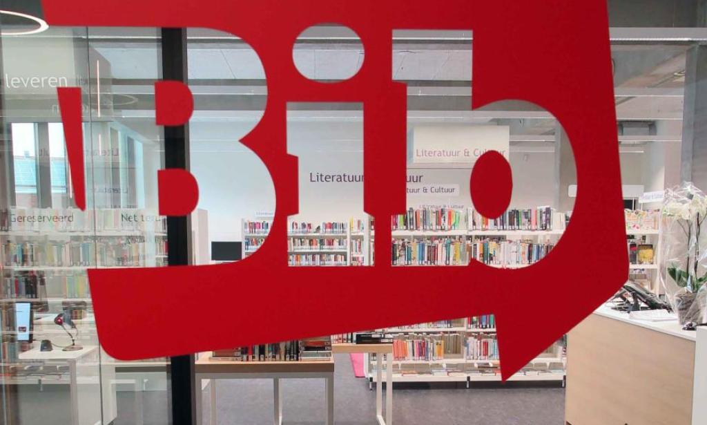 Op deze afbeelding van de Leo Pleysierbibliotheek zie je door het glas de boeken van de bib. Je ziet ook het logo van het bib op het glas.